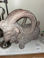 Large Billy Goat sculpture in neutral earthy tones next to metal fireplace tools and decorative plates.
