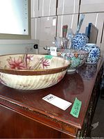 Overall image showing all items on a wooden table including floral bowls, blue and white vases, cranberry and clear glass vases.