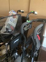 Photo showing Nexus rollator frame, padded handles, hand brakes, and front black mesh basket with items.