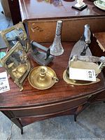 Overall view of the lot on a wooden table showing all items described by seller including sadirons, candle holder, bud vase, and mirrors.
