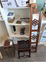 Photo showing two wooden plant stands and the decorative carved wooden panel leaning vertically on a white shelving unit.