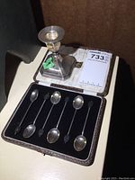 Set of six sterling spoons in fitted case and weighted sterling candle holder on top, showing all items together.