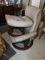 Recliner chair with ottoman cushion placed on seat, showing side profile of leather upholstery and wooden swivel base
