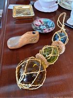 Two blown glass hanging balls in netting with cork tops beside a small wood handled tool and a small dish with floral pattern
