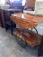 Photo of wood tea wagon showing detailed painted inlay, metal wheels, and metal handles. One piece of metal trim is unattached.