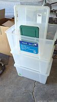 Stack of four translucent plastic storage totes, three large totes with lids and one smaller tote with lid at top of stack