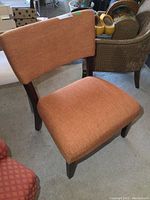 Front angled view of the modern upholstered chair showing orange fabric seat and backrest with dark wooden legs