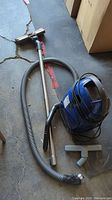 Blue Miele vacuum cleaner with attachments including a power head, metal wand, and two floor attachments on the floor.