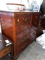 Full view of the vintage highboy dresser showing 8 drawers with brass handles, wood finish, and some surrounding items on top.