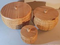 Three round wicker baskets with wood lids arranged side by side on a flat surface