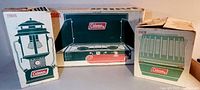Three boxed items including Coleman two-burner stove, lantern, and heater boxes.