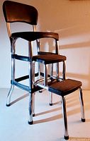 Side angled view showing chrome metal frame, two step design, brown upholstered seat and backrest, rubber tips on legs.