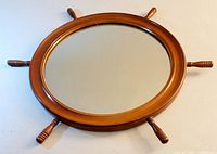 Image showing the entire oval wooden framed ship wheel mirror lying flat on a white surface, showcasing the six handles protruding evenly spaced.