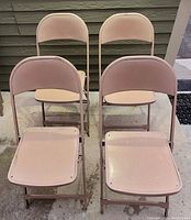 Four small beige metal folding chairs arranged in two rows, showing the front and side views. Chairs have metal frames and seats with visible surface wear and scratches.