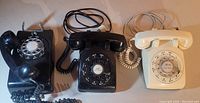 Wide view showing all three rotary dial telephones in black and white colors with cords and handsets.