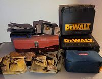 View of assorted tool cases (DeWalt hard cases, Ryobi bag, CLC tool roll), red metal toolbox, and two leather tool belts