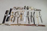 Image showing 19 women's wristwatches arranged in rows on a flat surface. Various strap materials and watch face shapes visible.