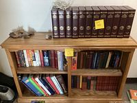 Oak wooden bookcase displaying assorted books and complete National Geographic bound volumes on top shelf.