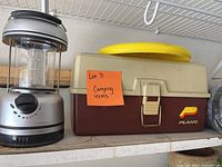 Front view of lantern and Plano tackle box on shelf with note 'Lot 71 Camping items'