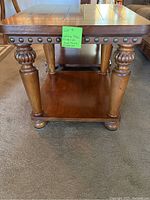 Wooden coffee/end table showing side view with decorative rounded legs, metal stud accents on apron, and lower shelf.
