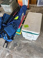 Lot of two blue folding chairs in bags, two white Igloo coolers and a green and yellow cooler on floor.