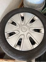 Full view of a tire mounted on a wheel with a silver plastic Mitsubishi branded hubcap, shows seven spokes and wear marks.