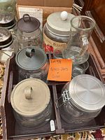 Photo of multiple glass jars with various lids including metal, ceramic and no lid, arranged in a brown tray.