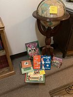 Globe on wooden stand positioned behind a group of children's books and a small notebook placed on the floor. Books include 'The Cat in the Hat' and others, colorful and visibly used.