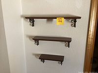 Three dark wood wall shelves mounted on wall with decorative metal brackets
