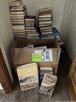 Stacks of assorted hardcover and paperback books with a box labeled misc books