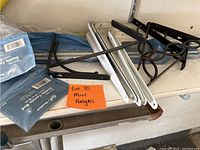 Photo of various curtain rod brackets and hangers including white metal brackets, black decorative metal hangers, and two unopened packs of King & Queens double curtain rod brackets in blue packaging.