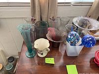 Twelve unique vases and decorative glass items arranged on a white surface near window light.