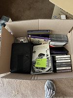 Box top view showing CDs and cassette tapes inside the box, some CD jewel cases and cassette tapes visible.