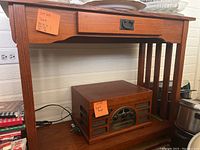 Full view of the wooden table showing its drawer and open shelf with a vintage radio on the bottom shelf.