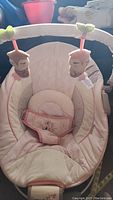 Pink baby sleeper rocker with quilted cream and pink fabric and toy bar showing two owl plush toys.
