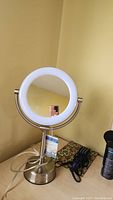 Full view of the vanity mirror showing round illuminated mirror and metal stand on table.