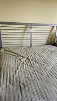Photo showing queen size metal bed frame headboard with horizontal slats and part of mattress covered with wrinkled beige sheet.