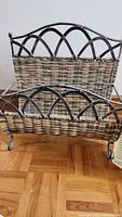 Photo of a weaved book or magazine holder with a curved metal frame and woven wicker basket section.