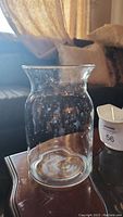 Clear round glass vase on a wooden table with a couch background. Shows some water spots and residue needing cleaning.
