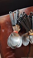 Close up photo showing a bunch of table spoons with black handles and stainless steel spoon heads tied together with a red rubber band.