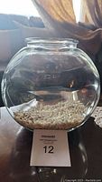 Front view of clear glass fish bowl with white decorative rocks at the bottom, showing round shape and wide opening.