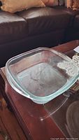 Photo showing clear square glass bakeware dish on wooden table, needs cleaning.