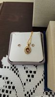 Gold-tone necklace with oval brown stone pendant and matching stud earrings shown on white cushion