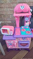 Front view of Minnie Mouse pink and purple play kitchen with microwave, stove burners, oven, and Minnie decor