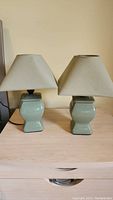 Pair of green ceramic night stand lamps on a wooden dresser, showing front and side views.