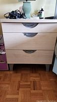 Front view of night table showing three drawers with metal handles and damaged top surface; items on top not included