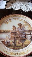 Close-up photo showing the painted scene on the decorative plate and part of a lace doily underneath.