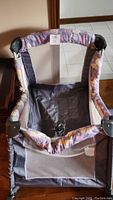 Gray and purple girl playpen frame with fabric padded sides featuring butterfly prints. View shows the interior with netted side storage pocket.