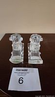 Two clear glass carved horse shapes or rocking horse element figurines shown from the front on a dark surface.