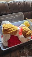 Stuffed animals inside clear Sterilite plastic bin, showing brown and white dog with pink collar and yellow duck